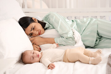 Young woman with her baby suffering from postnatal depression on bed in bedroom