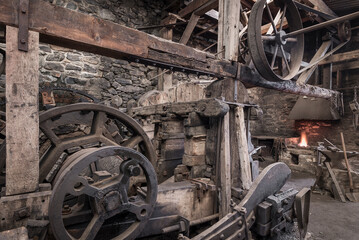 Historic machinery in a blacksmiths worksshop. - obrazy, fototapety, plakaty