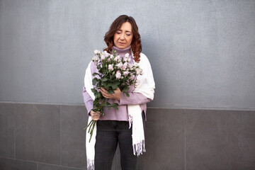 A beautiful middle-aged woman keeps a bouquet of beautiful flowers, purple roses. The girl walks...