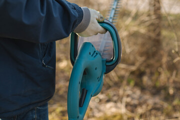 Close-up of a man holding an electric brush cutter to cut off the branches in the garden on a...