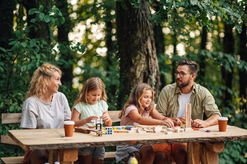 Sisters playing fun board game in nature while parents watching.