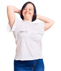 Brunette woman with down syndrome wearing casual white tshirt relaxing and stretching, arms and hands behind head and neck smiling happy