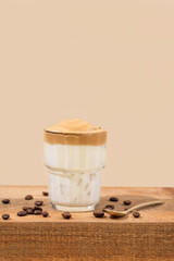 Dalgona coffee. Whipped instant coffee in a glass on a wooden table with coffee beans on a beige...