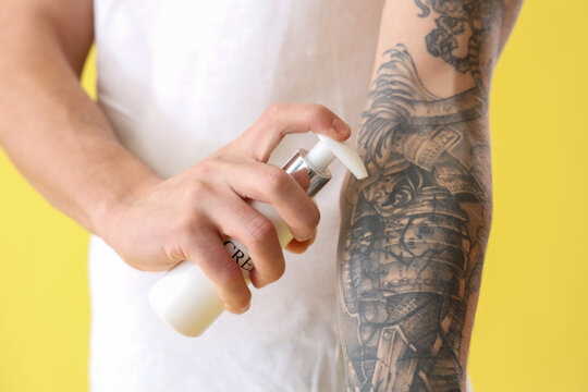 Young man applying tattoo cream on yellow background, closeup