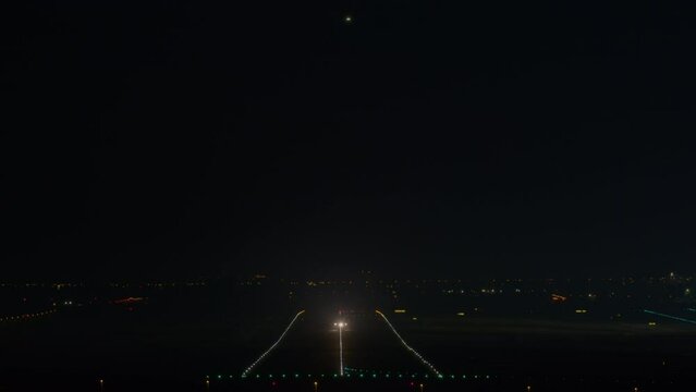 Two airplanes in different flight phases - one high with landing lights on for descent, another close, lifting off from a brightly lit runway