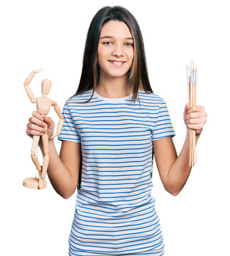 Young brunette girl with long hair holding small wooden manikin and pencils smiling with a happy and cool smile on face. showing teeth.