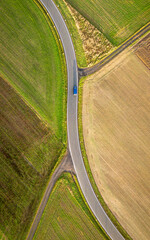 Top down view of a blue car driving between the fields on the country road
