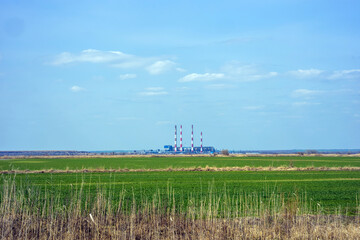 Power plant against the sky, beautiful landscape against the background of blue sky and green field.