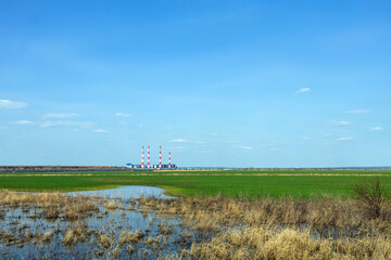 Exterior view of a thermal power plant against a background of a green field under a blue sky