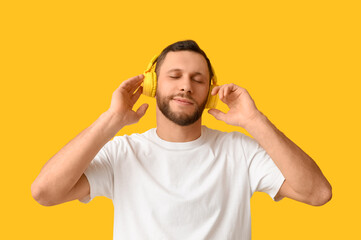 Young man in modern headphones on yellow background - 775306725