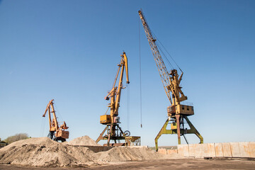 Fototapeta na wymiar Port industrial cranes at river sand unloading depot on clear sunny day