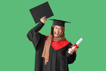 Muslim female graduate student with diploma throwing mortar board up on green background