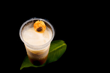 Iced latte coffee on plastic cup and isolated black background with sprinkles of cookies, summer...