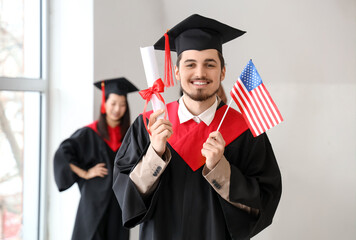 Male graduate student with diploma and USA flag in light room