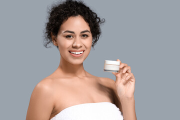 Young African-American woman with jar of facial cream on grey background, closeup