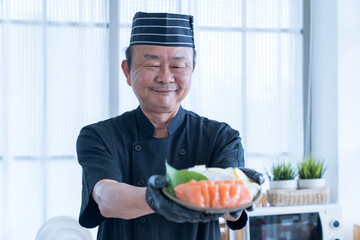 The salmon slice is in the hands of the chef. Asian chef slice salmon by knife.