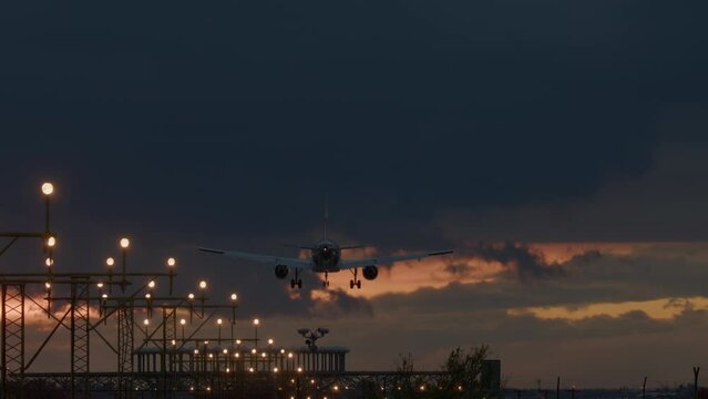 Airplane with landing gear extended flying low over runway lights at dusk