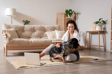 Sporty young African-American woman with cocker spaniel sitting after training at home