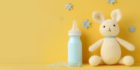 Cute baby product banner, knitted toy and baby bottle laying on tender yellow background with copy space.