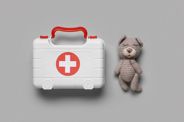 Toy first aid kit with teddy bear on grey background. Top view