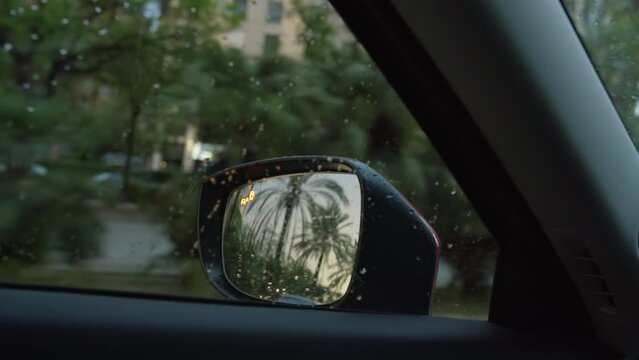 View from inside the car, raindrops on the window and the taillights of a passing car reflected in the side mirror