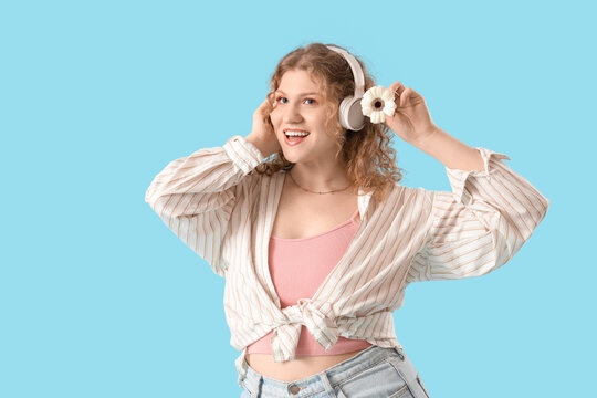 Fototapeta Pretty young woman in headphones with beautiful gerbera flower on blue background