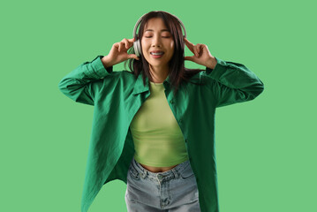 Asian young woman listening music in headphones on green background - obrazy, fototapety, plakaty