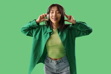 Poster Asian young woman listening music in headphones on green background © Pixel-Shot
