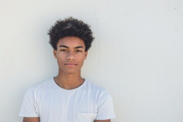 Teenage boy with curly hair portraying neutrality against a plain white background - obrazy, fototapety, plakaty
