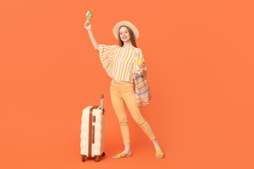 Happy young woman with suitcase, passport and ticket on orange background. Travel concept
