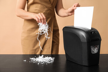 Secretary destroying document in shredder on beige background
