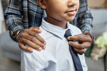 Close up of unrecognizable caring father tying tie for son dressing up