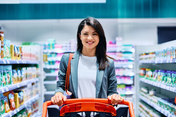Happy woman with shopping cart at supermarket looking at camera.