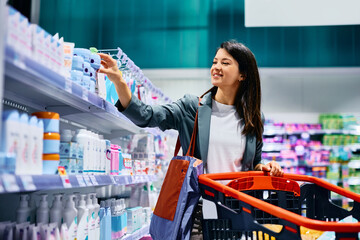Happy woman choosing moisturizer while shopping at supermarket.