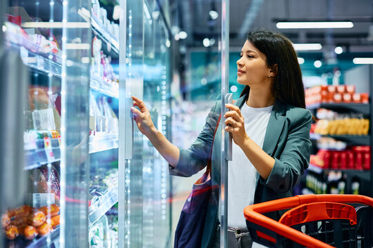Smiling woman buying groceries at refrigerated section in  supermarket.