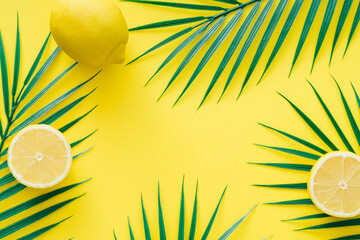 Creative trendy summer composition made with lemons and tropical green palm leaves on bright yellow...
