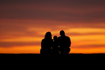 Silhouette of couple with child against vibrant sunset sky