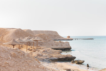 Minimalistic calm travel background with lonely small house and the ruined pier. Sandy and rocky coast in Egypt. Desolate beach on the coast shore of Red Sea. Pastel colors. Concept of pacification.