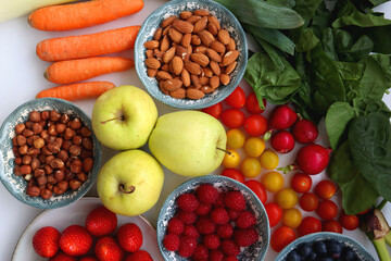 Apples, lemons, bananas, berries, carrots, leek, tomatoes, radishes, spinach and various nuts on white background. Healthy seasonal fruit and vegetable. Top view.