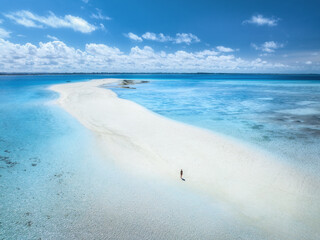 Aerial view of alone young woman on the sandbank in ocean, white sand, blue sea during low tide at sunny summer day in Nakupenda, Zanzibar island. Top view of girl, sand spit, water, sky with clouds