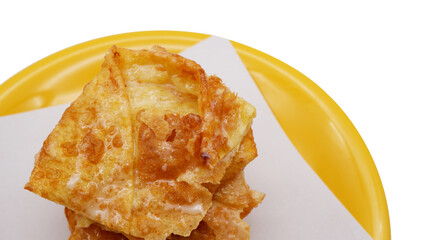 Fried roti on a yellow plate isolated on a white background. Crispy Thai roti is one of the Thai street desserts with sweetened condensed milk with a crispy texture. Roti texture with copy space.