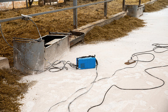 The welding machine is connected to the iron railings of the animal enclosures in the barn.