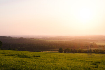 Sonnenuntergang über grüner Landschaft mit Dunst am Horizont