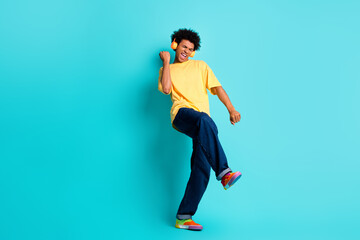 Fototapeta na wymiar Full length photo of good mood funky guy dressed yellow t-shirt in headphones clenching fist isolated on turquoise color background
