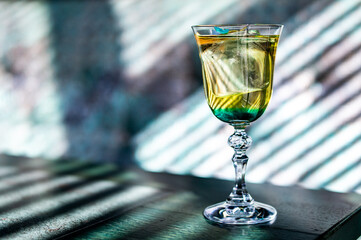A refreshing iced beverage in an elegant glass, casting dramatic shadows on a dark wooden surface....