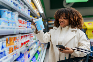 With a basket in hand a beautiful curly hair black woman searching and buying groceries in super...