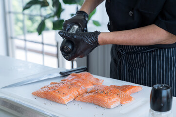 Asian chef cutting salmon by knife. Man cutting raw salmon and Sprinkle with black pepper.