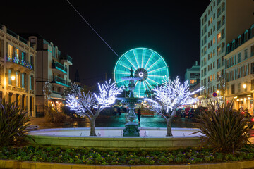 Manège grande roue devant une fontaine illuminée en bleu dans une ville la nuit