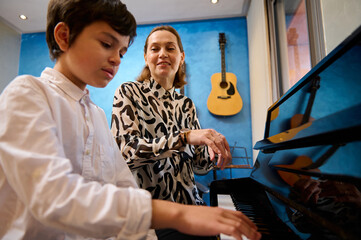 Teenager student boy sitting at piano near her teacher, having piano lesson at home. Different...