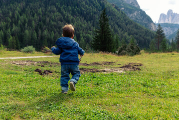 Naklejka na ściany i meble Child running on a mountain meadow with a bell in his hand. Summer holidays in the mountains, blue jacket